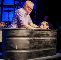 a man is holding a woman in a tub on stage