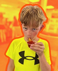 a young boy eating a hot dog in a classroom