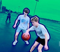 two young men playing basketball in a parking lot